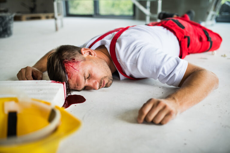 An unconscious man worker lying on the floor after an accident on the construction site, blood on head.